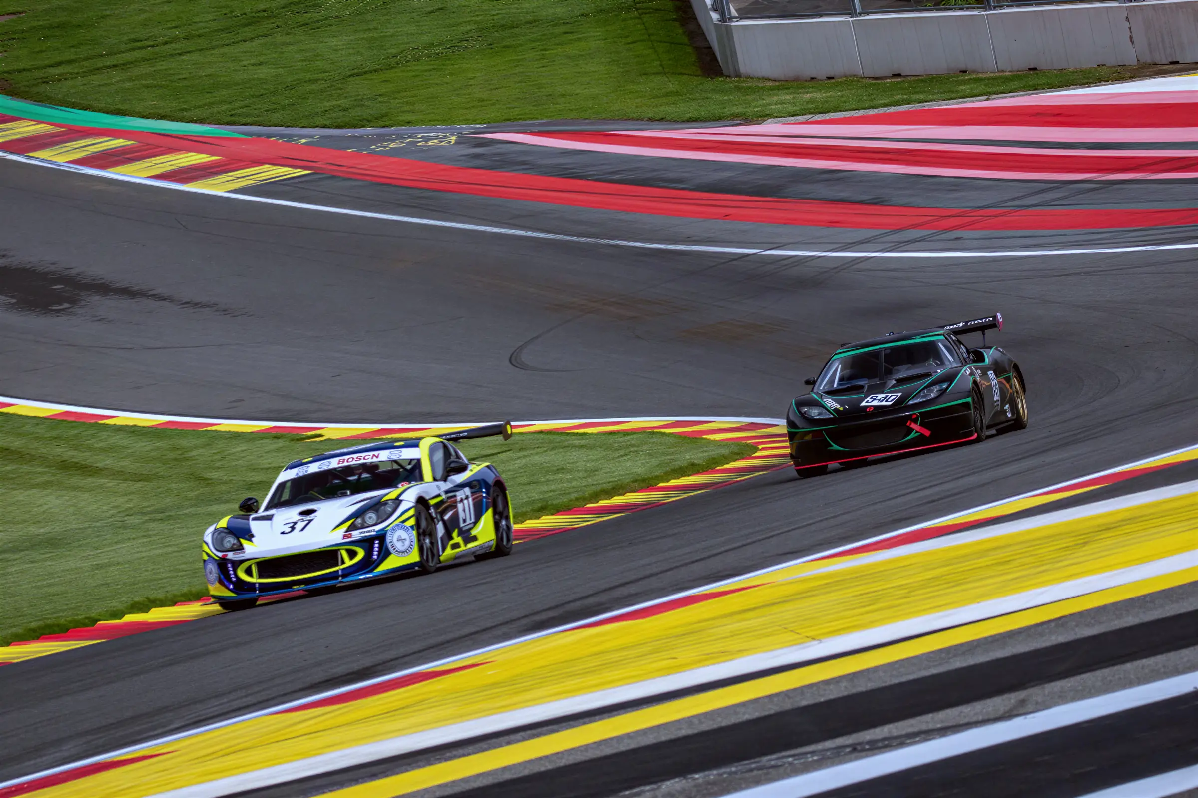 Lotus Evora GT4 číslo 540 v černo-zelené na trati Spa-Francorchamps, před ní žlutá Ginetta, květen 2026